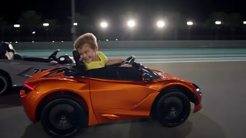 Criança sorrindo ao volante de um carrinho elétrico laranja, numa pista iluminada à noite.