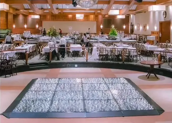 Salão do Espaço Augusta com mesas postas, lustres e a pista de dança iluminada em primeiro plano.