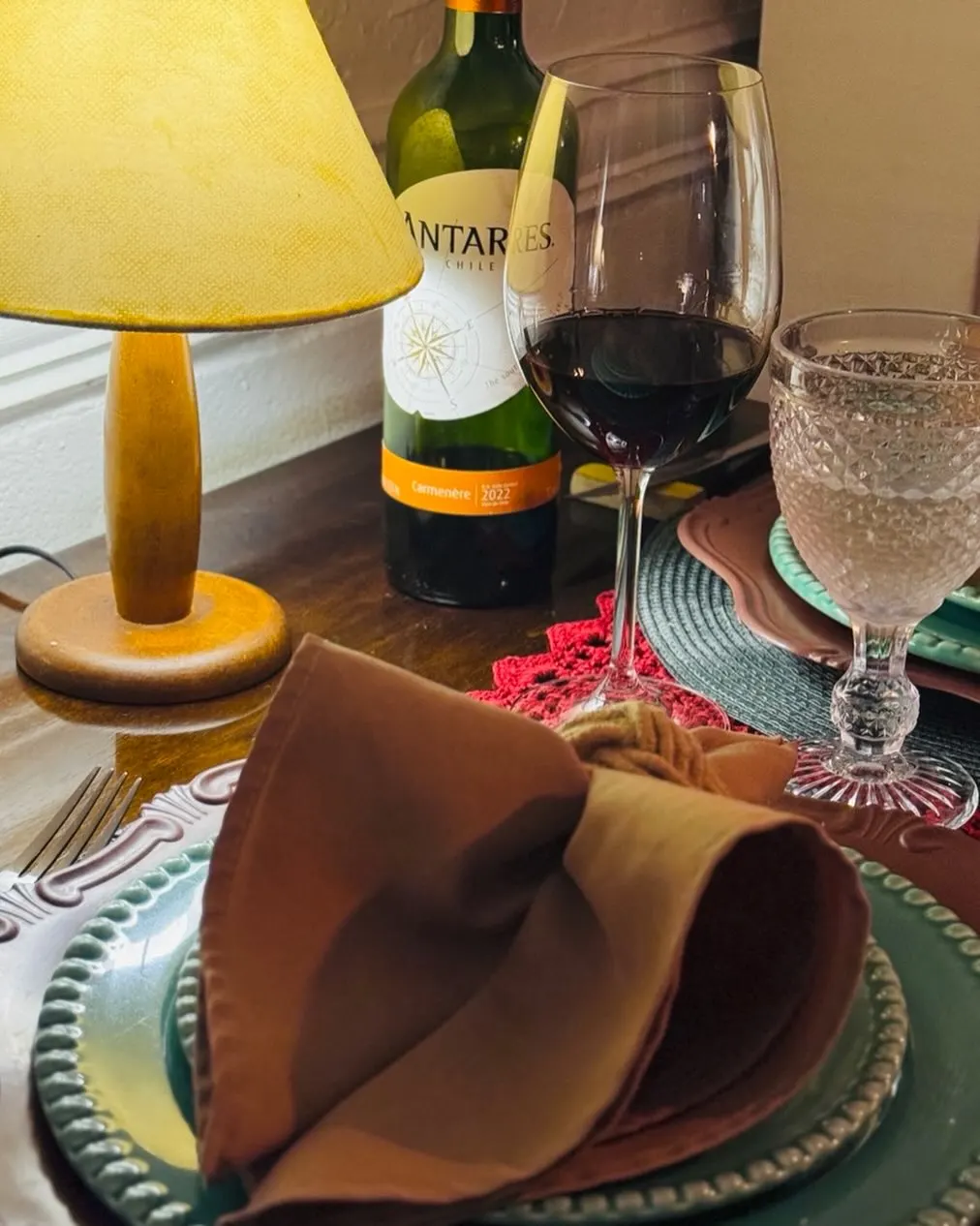 Mesa à luz do abajur, com taças e garrafa de vinho.